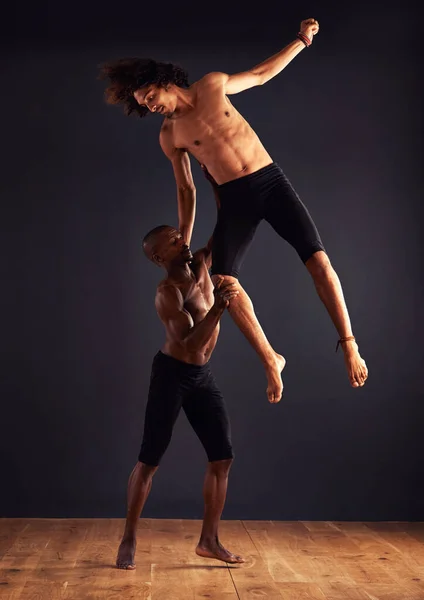 彼が飛ぶのを助ける力。暗い背景の前で二人の男性現代ダンサーが劇的なポーズをとる. — ストック写真