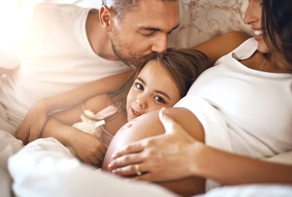 Theres enough love for one more. Shot of a happy little girl lying in bed with her dad and pregnant mother. — Stock Photo, Image