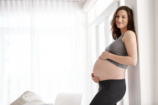 Promieniowanie instynktem macierzyńskim. Portret młodej kobiety w ciąży stojącej w swoim domu. — Zdjęcie stockowe