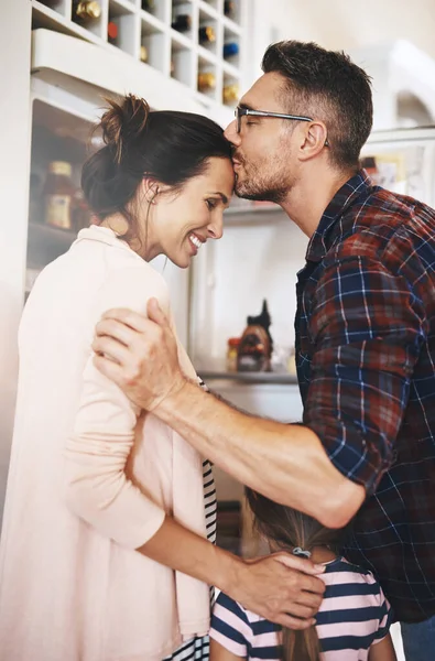 Ele aprecia-a. Tiro de um marido amorosamente beijando sua esposa na cozinha com sua família. — Fotografia de Stock