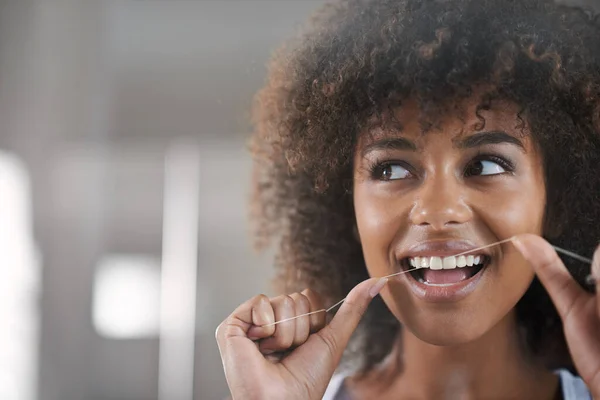 Ela gosta muito de higiene dentária. Tiro de uma jovem mulher que usa fio dental nos dentes no espelho. — Fotografia de Stock