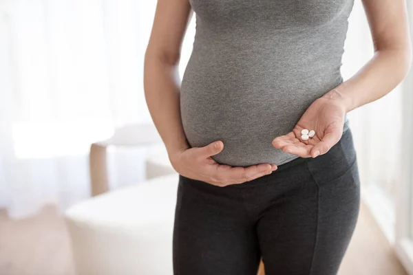 Prenatale vitaminen. Gehakt schot van een zwangere vrouw die tabletten vasthoudt terwijl ze in haar huis staat. — Stockfoto