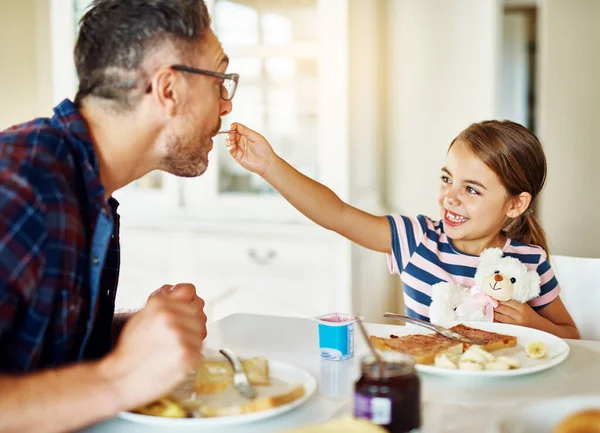 Goûtez le mien. Plan recadré d'une adorable petite fille prenant le petit déjeuner avec son père dans la cuisine. — Photo