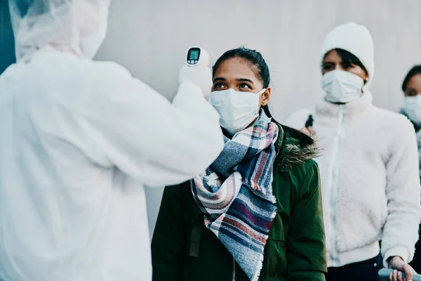 By zapewnić bezpieczeństwo obywatelom. Strzał młodej kobiety mierzącej temperaturę termometrem na podczerwień przez pracownika służby zdrowia podczas wybuchu epidemii. — Zdjęcie stockowe