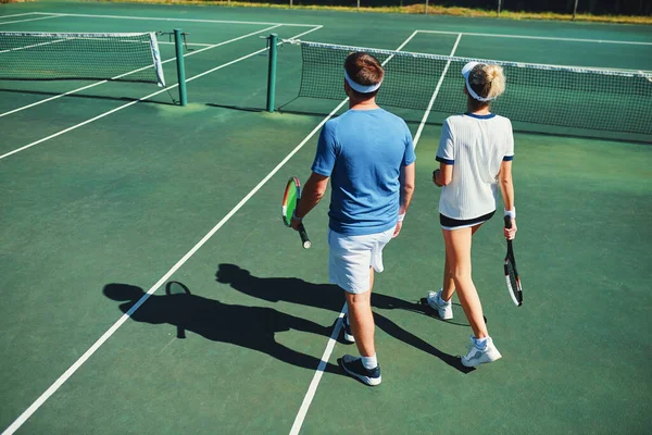 We zijn altijd klaar voor de uitdaging. Full length shot van twee jonge tennissers praten tijdens het wandelen samen buiten op een tennisbaan. — Stockfoto