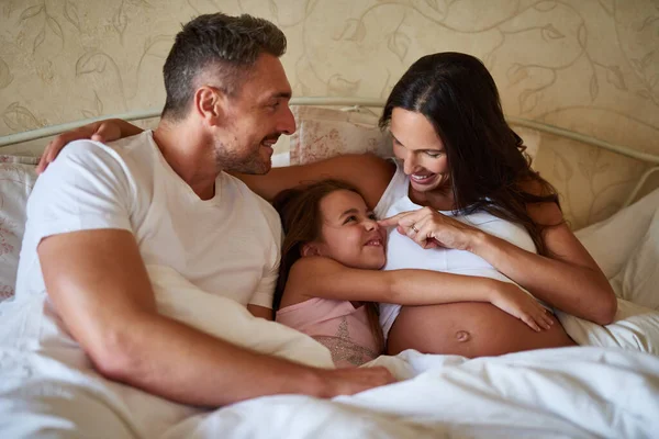 And soon there will be four. Shot of a happy little girl lying in bed with her dad and pregnant mother. — Stock Photo, Image