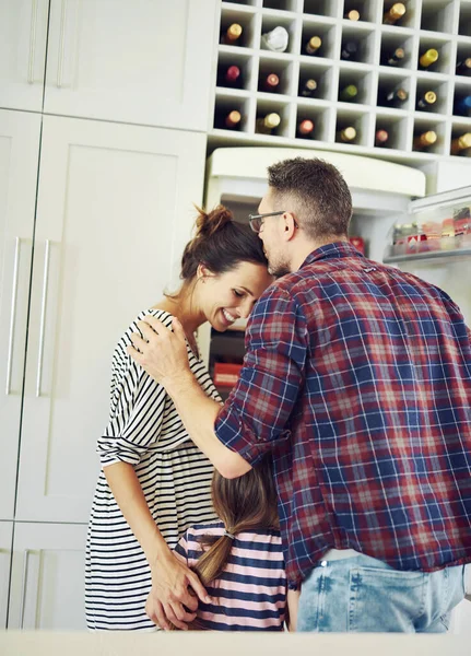 Juntos pelo amor. Tiro de um marido amorosamente beijando sua esposa na cozinha com sua família. — Fotografia de Stock