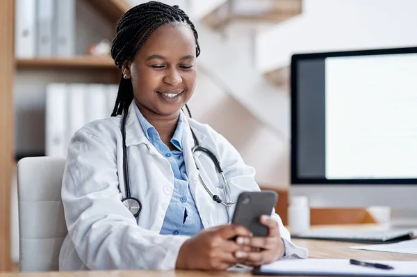 Ze verwelkomt berichten van haar patiënten. Shot van een jonge arts met behulp van een mobiele telefoon tijdens het werken in haar kantoor. — Stockfoto