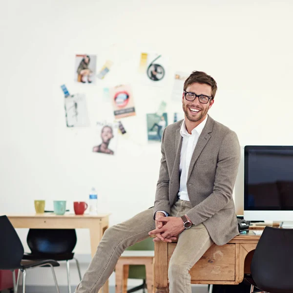 Ik hou echt van mijn werk. Portret van een casual geklede jongeman zittend op zijn bureau in een kantoor. — Stockfoto