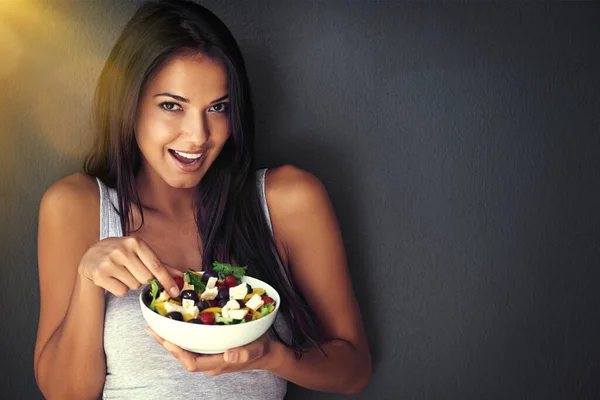 Gör kroppen bra. Porträtt av en frisk ung kvinna som äter en sallad mot en grå bakgrund. — Stockfoto