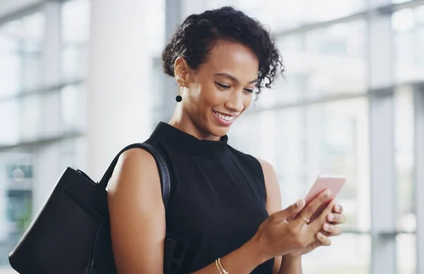 Olumlu bir mesaj yolluyorum. Modern bir ofiste yürürken akıllı telefon kullanan ve el sallayan genç bir iş kadınının görüntüsü.. — Stok fotoğraf