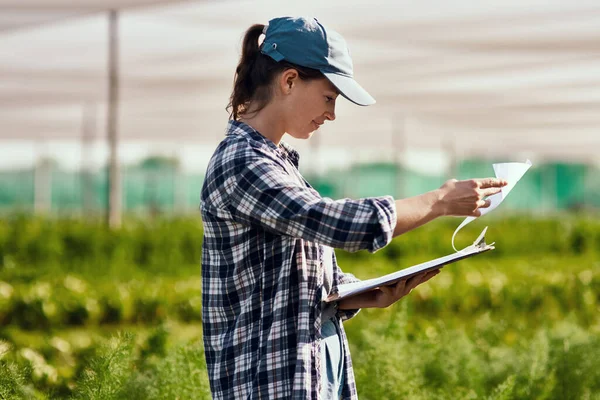 Estes números parecem promissores. Tiro colhido de uma jovem agricultora atraente olhando sobre a papelada enquanto trabalhava em sua fazenda. — Fotografia de Stock