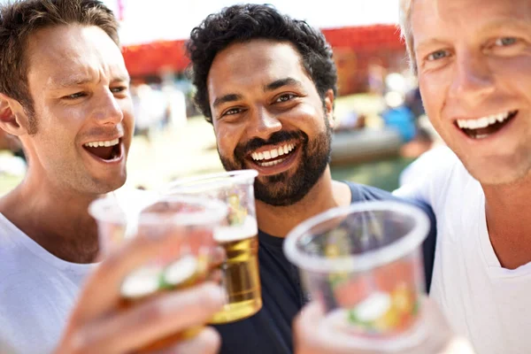 Nu sätter vi igång festen. Tre unga män skålar sina öl på en musikfestival. — Stockfoto
