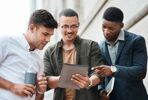 Blijf verbonden met ambitieuze mensen. Foto van een groep jonge zakenmannen die samen een digitale tablet gebruiken tegen een stedelijke achtergrond. — Stockfoto