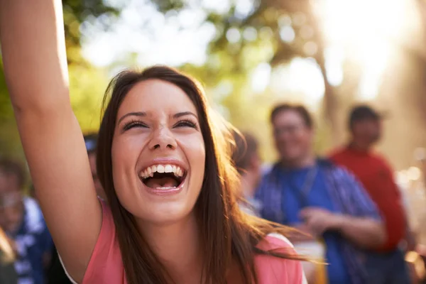 C'est une fière partisane. Une belle jeune femme souriante et jouissant de musique lors d'un festival avec le bras levé en l'air et la foule en arrière-plan. — Photo