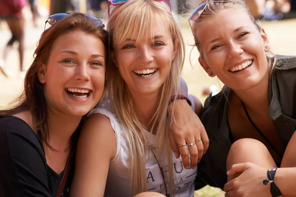 Hanging out with the girls. Portrait of three smiling friends sitting arm in arm and at a festival. — Stock Photo, Image