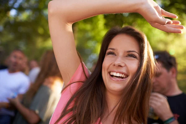 Profiter du divertissement. Une belle jeune femme souriante et jouissant de musique lors d'un festival avec le bras levé en l'air et la foule en arrière-plan. — Photo