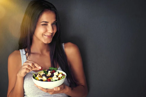 Du kommer att älska det här. Porträtt av en frisk ung kvinna som äter en sallad mot en grå bakgrund. — Stockfoto