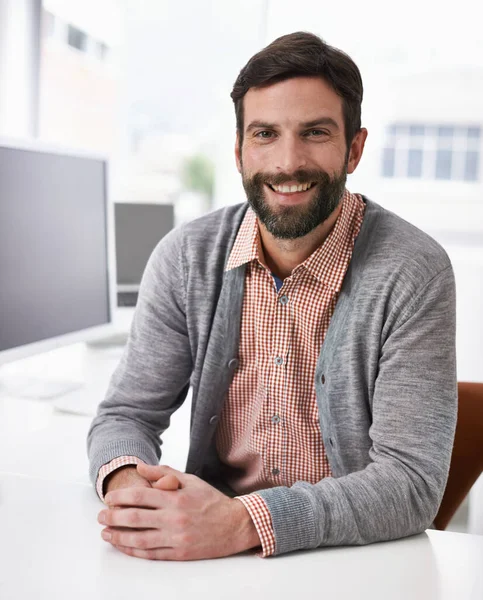 Inhoud in mijn werkomgeving. Een trendy zakenman zit aan zijn bureau en glimlacht naar de camera. — Stockfoto