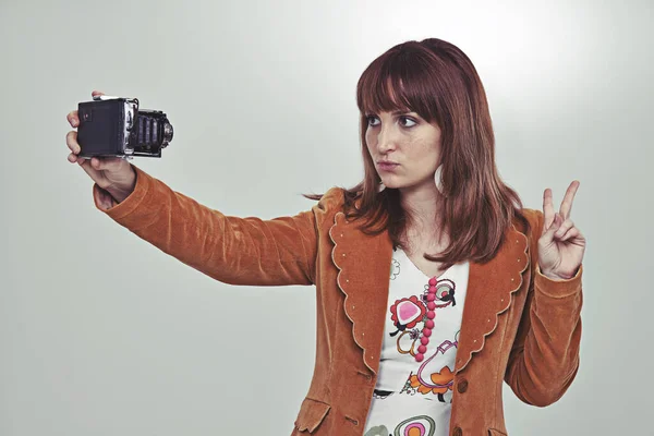 Das Selfie der Siebziger. Ausgeschnittene Studioaufnahme einer jungen Frau im Vintage-Outfit, die ein Selfie mit einer altmodischen Kamera macht. — Stockfoto
