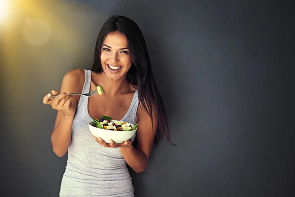 Friska och läckra. Porträtt av en frisk ung kvinna som äter en sallad mot en grå bakgrund. — Stockfoto