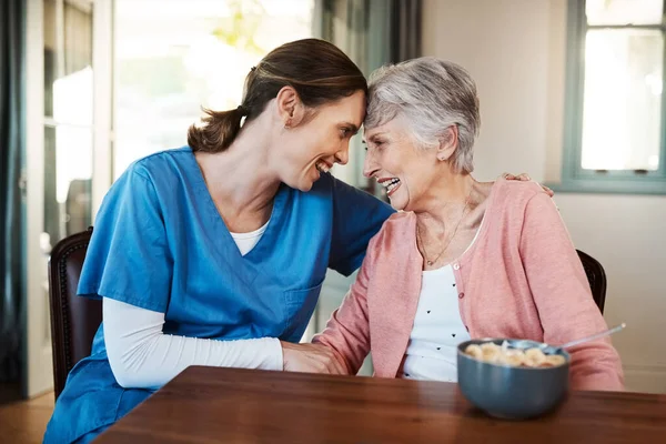 患者さんの幸せが第一です。老人ホームで朝食時に先輩女性と座っている若い看護師のショット. — ストック写真