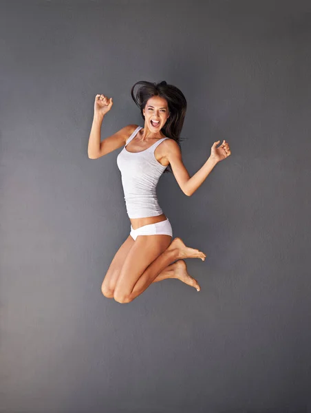 人生をエキサイティングにしなければならない。フル長いですショットの幸せな若い女性ジャンプに対して灰色の背景. — ストック写真