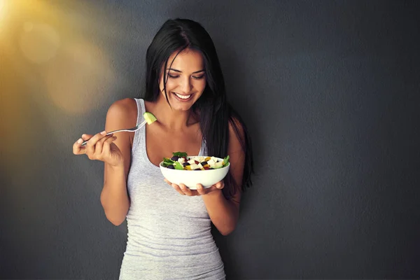 Isto é delicioso. Tiro de uma jovem saudável comendo uma salada contra um fundo cinza. — Fotografia de Stock