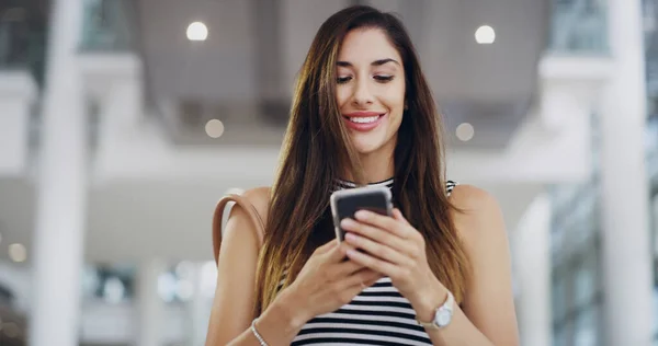 Las herramientas modernas para la empresaria moderna. Recorte de una joven mujer de negocios usando un teléfono inteligente mientras camina a través de una oficina moderna. —  Fotos de Stock