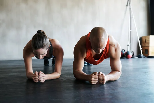 Empuje su camino a la aptitud. Tiro de un hombre y una mujer haciendo ejercicios de tablón en el gimnasio. — Foto de Stock