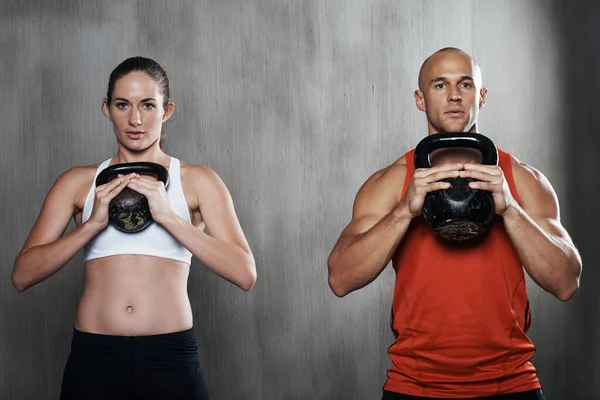Están comprometidos a mantenerse en forma. Un hombre y una mujer haciendo ejercicio con campanas de caldera en el gimnasio. —  Fotos de Stock