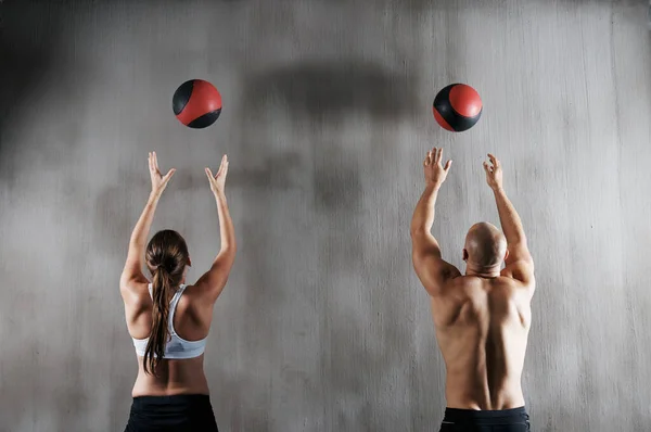 Entrenamiento para convertirse en combate en forma. Tiro de un joven y una mujer haciendo ejercicio con pelotas de medicina en el gimnasio. — Foto de Stock