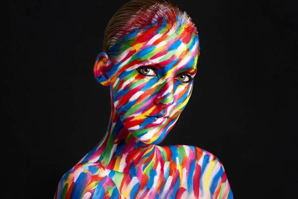 Atractivo, llamativo belleza colorida. Foto de estudio de una joven posando con pintura de colores brillantes en su cara sobre un fondo negro. —  Fotos de Stock