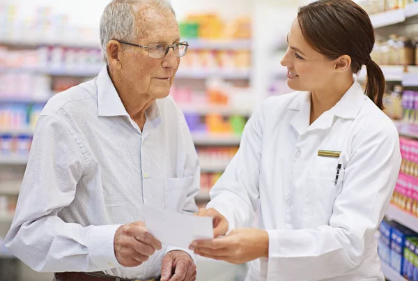 Explaining prescriptions in plain language. Shot of a young pharmacist helping an elderly customer with his prescription. — Stock Photo, Image