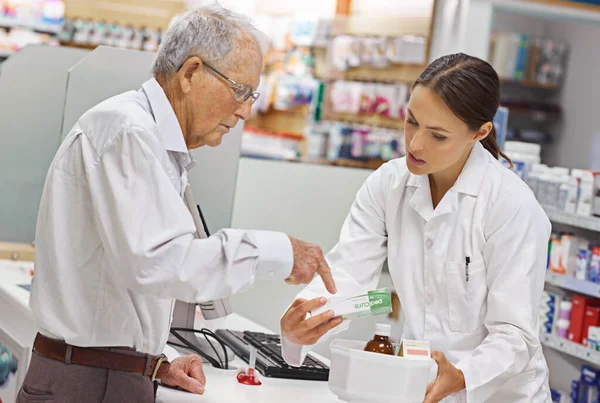 Siempre está ahí para consultas de clientes. Inyección de un joven farmacéutico ayudando a un cliente mayor en el mostrador de prescripción. —  Fotos de Stock