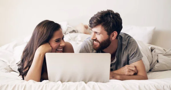 Lata morgnar online. Skjuten av ett lyckligt ungt par med hjälp av en bärbar dator medan du kopplar av på sängen hemma. — Stockfoto