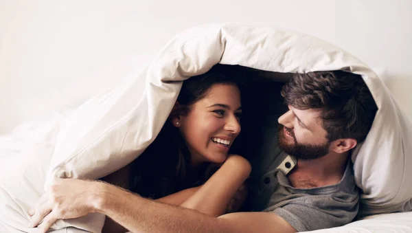 Gör plats för avkoppling. Skjuten av ett lyckligt ungt par som täcker sig med en filt på sängen hemma. — Stockfoto
