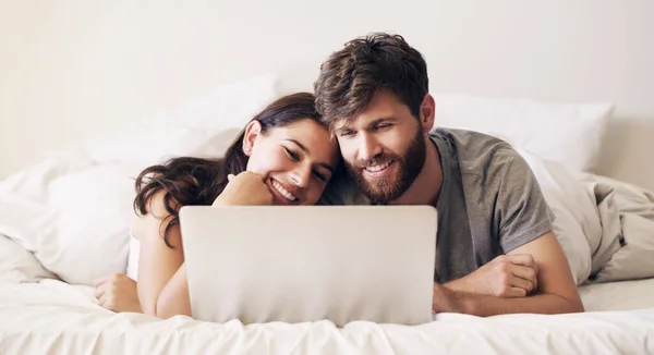 Spara lite tid varje dag för att ansluta. Skjuten av ett lyckligt ungt par med hjälp av en bärbar dator medan du kopplar av på sängen hemma. — Stockfoto