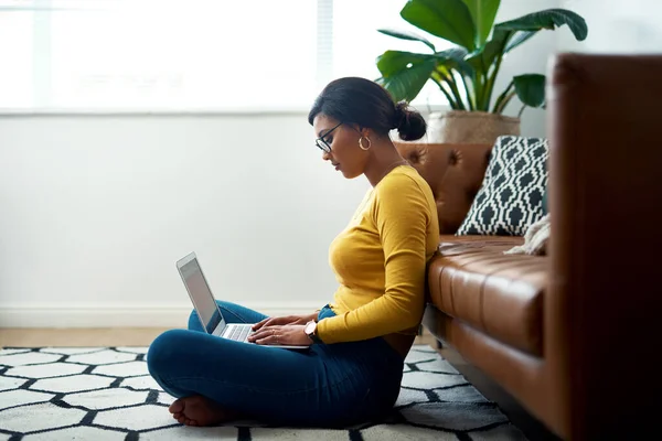 Die Freuden der Arbeit von zu Hause aus. Schnappschuss einer attraktiven jungen Frau, die im Schneidersitz auf dem Boden sitzt und ihren Laptop zu Hause benutzt. — Stockfoto