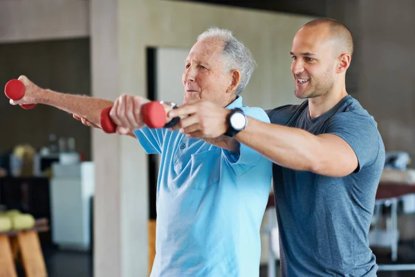 Довгий шлях до фізичної реабілітації. Знімок фізіотерапевта, який допомагає старшому чоловікові з вагами . — стокове фото