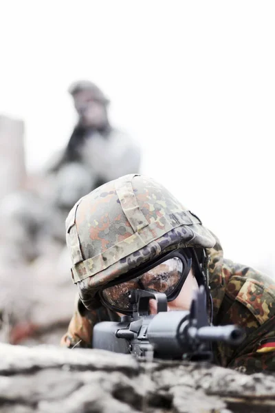 士兵躺在地上。一名士兵在堆积如山的石堆上窥视，用枪对着摄像机，并在镜头前放上抄袭空间。. — 图库照片