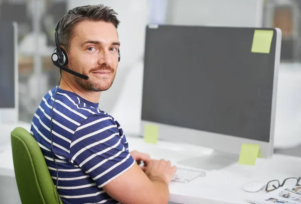 He handles customers like a pro. Shot of a young businessman wearing a headset while working at his desktop computer. — Stock Photo, Image