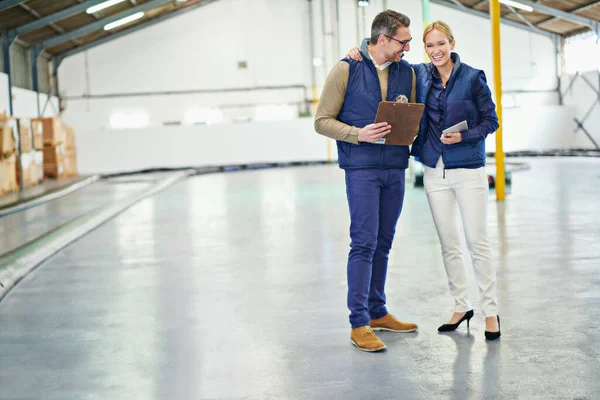 在庫リストを比較する。大規模な倉庫に立っている間に話している2人の同僚のショット. — ストック写真