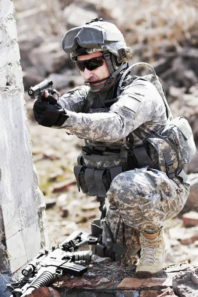 Getraind in de strijd. Een soldaat hurkte naast een kapotte muur en richtte zijn pistool in de verte.. — Stockfoto