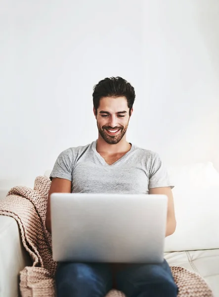 Spojeno tím nejpohodlnějším způsobem. Snímek mladého muže využívajícího bezdrátovou technologii na pohovce doma. — Stock fotografie