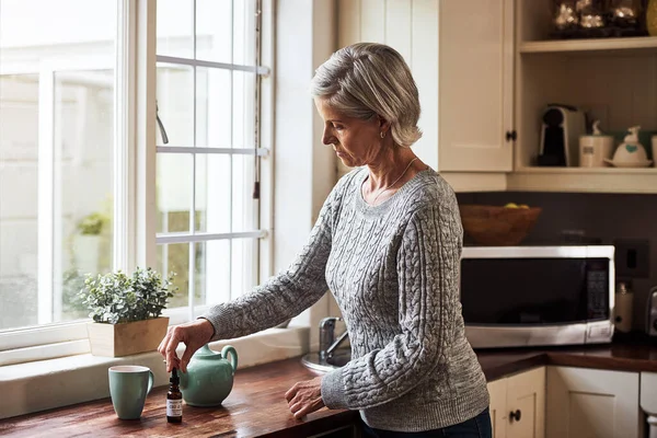 Time to take my medicine. Cropped shot of a relaxed senior woman preparing a cup of tea with CBD oil inside of it at home during the day. — Stock Photo, Image