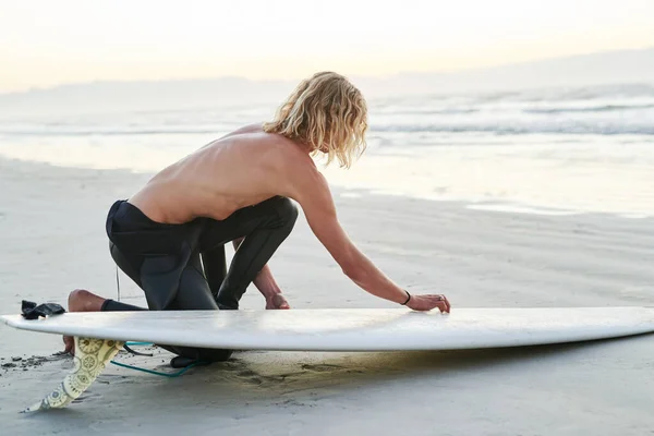 Minden készen áll. Teljes hossz felvétel egy jóképű fiatal szörfösről, aki szörfdeszkát készít, mielőtt szörfözik a strandon.. — Stock Fotó