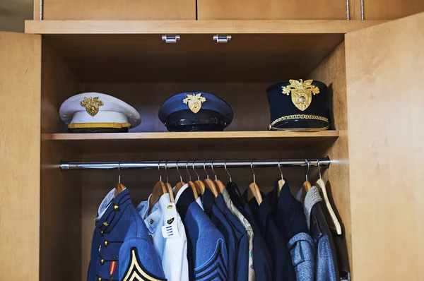No todos los héroes llevan una capa. Disparo de varias chaquetas militares y sombreros colgando en un armario. — Foto de Stock