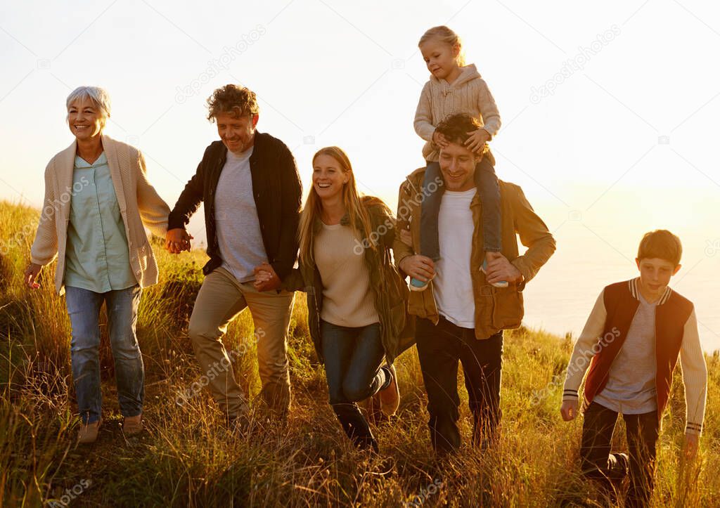 Together every step of the way. A multi-generational family walking up a grassy hill together at sunset.