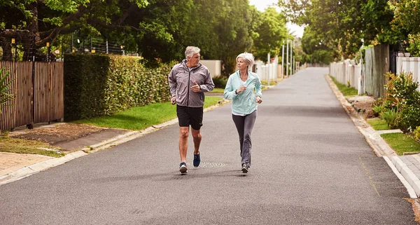 Probeer bij te blijven. Shot van een vrolijke senior paar met een jog samen buiten in een buitenwijk. — Stockfoto
